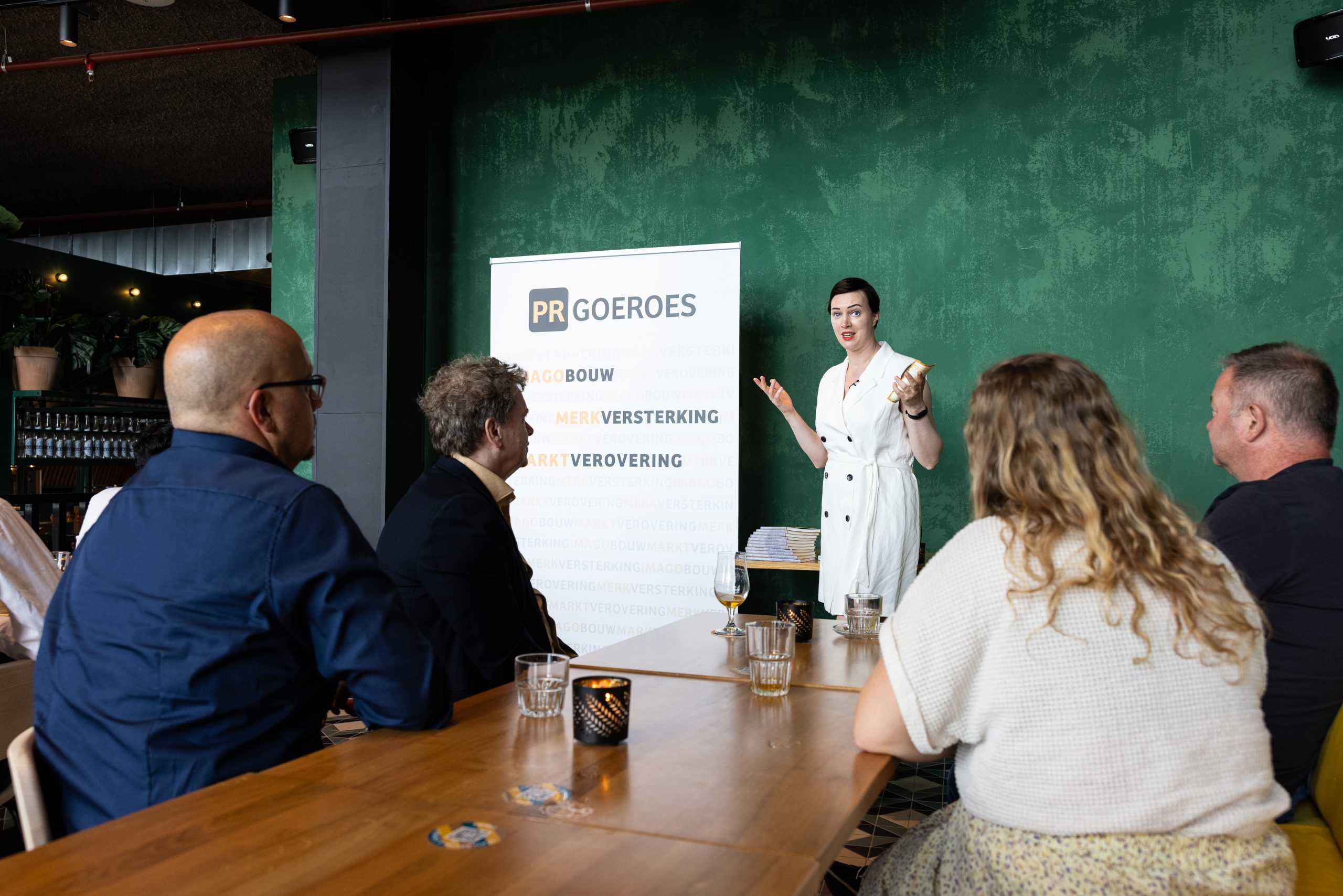 Wie is het beste PR-bureau van Nederland? Jennifer Delano, founder van PR-goeroes, geeft een presentatie aan een groep in een vergaderruimte en licht de strategische aanpak van het bureau toe.
