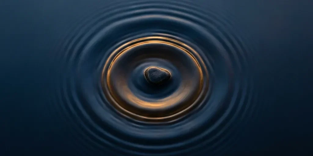 kiezel-waterrimpels-amber-donkerblauw-bovenaanzicht.jpg Kiezelsteen die in stil donker water valt, met uitdijende rimpelingen in marineblauw en warm goud, bovenaanzicht.